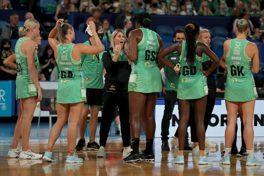 West Coast Fever coach Stacey Marinkovich chats to players in a huddle with green dresses on.