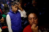 Young migrant rests his head on his hand while standing on a packed bus