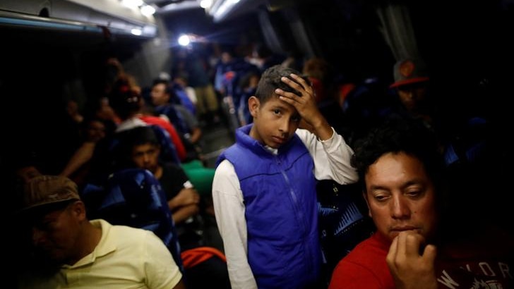 Young migrant rests his head on his hand while standing on a packed bus