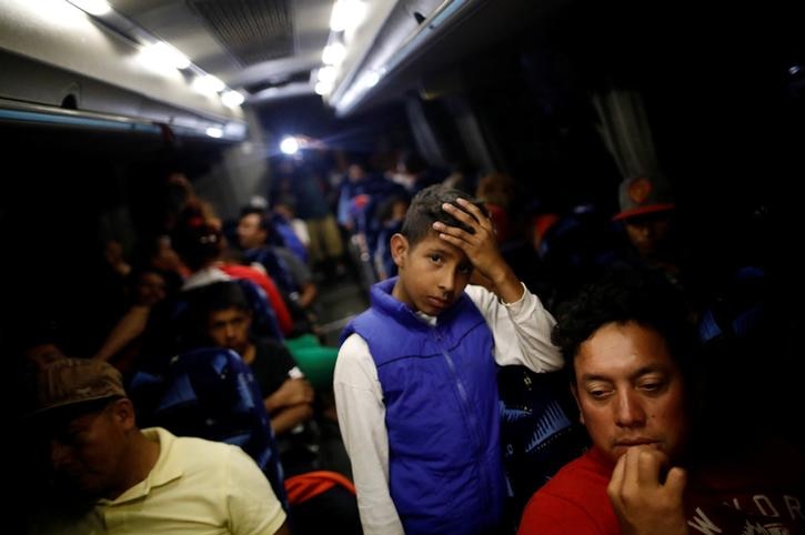 Young migrant rests his head on his hand while standing on a packed bus
