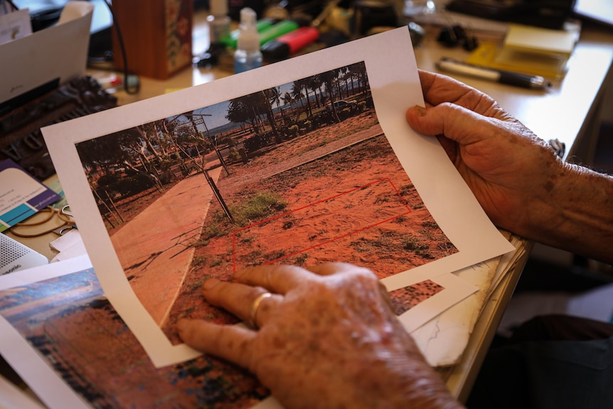 A photo of a plot in a cemetery which has been printed on paper is examined by an elderly man's hands.