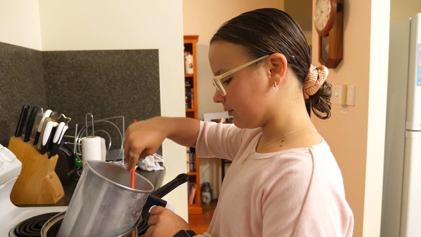 young girl in the kitchen with pots and pans stirring something