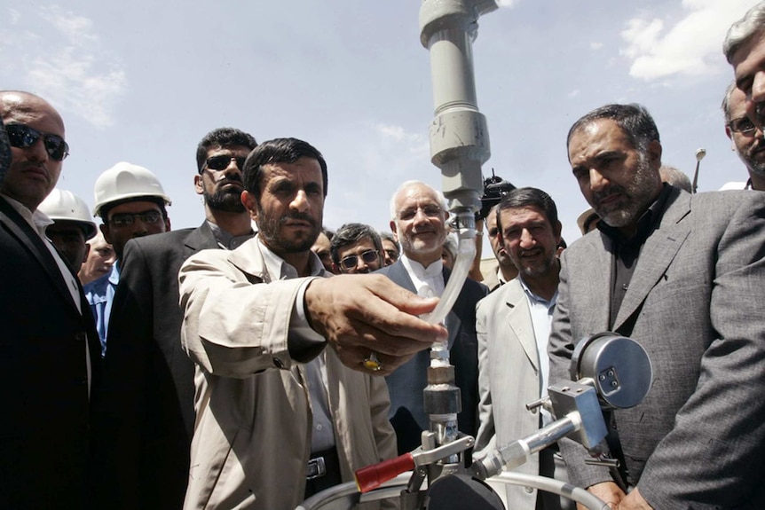 Mahmoud Ahmadinejad is surrounded by people watching him inspect a mechanism at the heavy water plant in Arak.