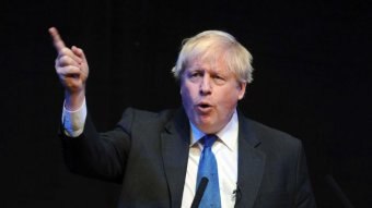 Boris Johnson gestures with one finger as he gives a speech against a black background.