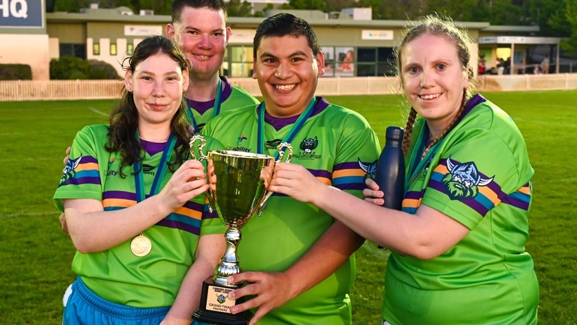four people in green football jerseys, pose with gold cup