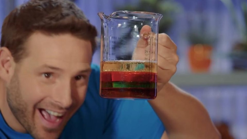 Smiling man looks at liquid in layers within a glass beaker