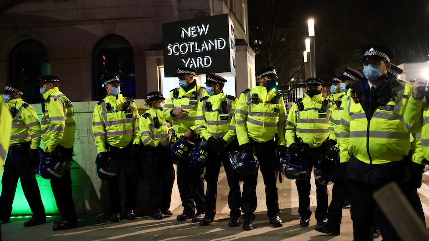 A large group of police in high-vis jackets stand outside New Scotland Yard