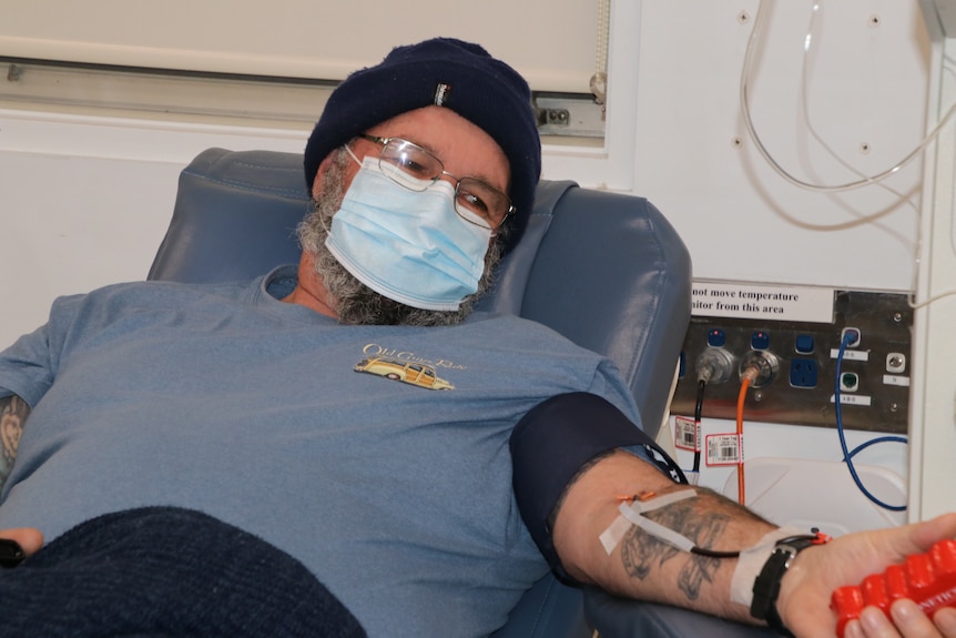 Steven lies on a medical bed, squeezing his fist while tubes are attached to his arm.