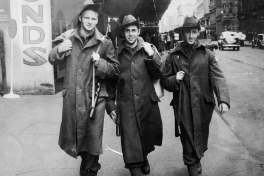 Three WWII soldiers walk down a street.