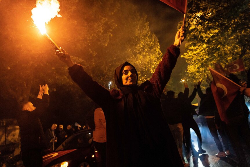 A woman holds up a flare at night 