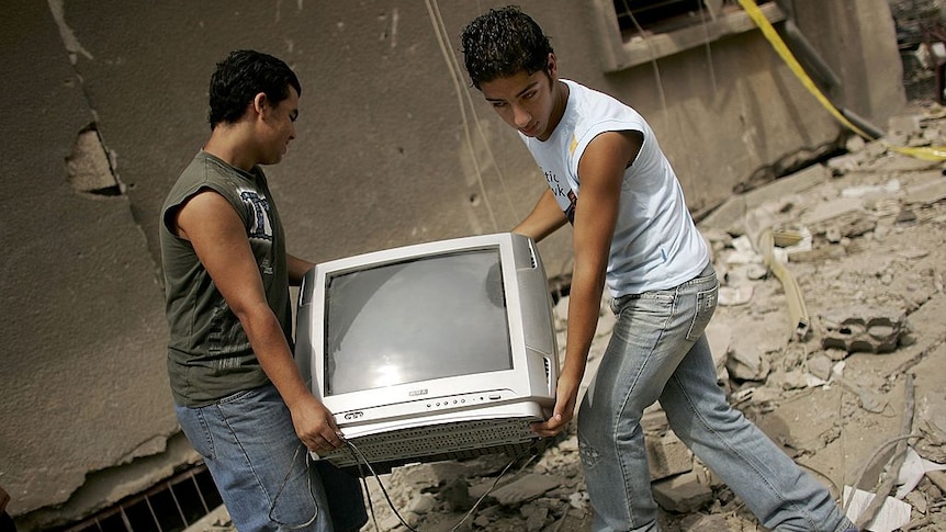 Two men carrying a television set over a pile of rubbish.
