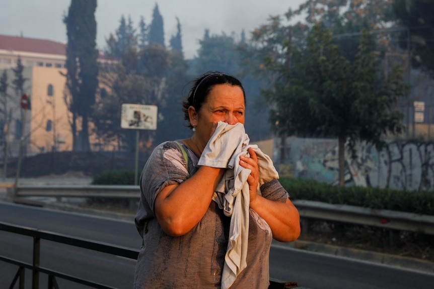 A woman holds a cloth over her face with smoke haze in the background. 