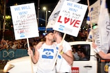Two men kiss while holding a sign which says 'Calm down, it's just love.'