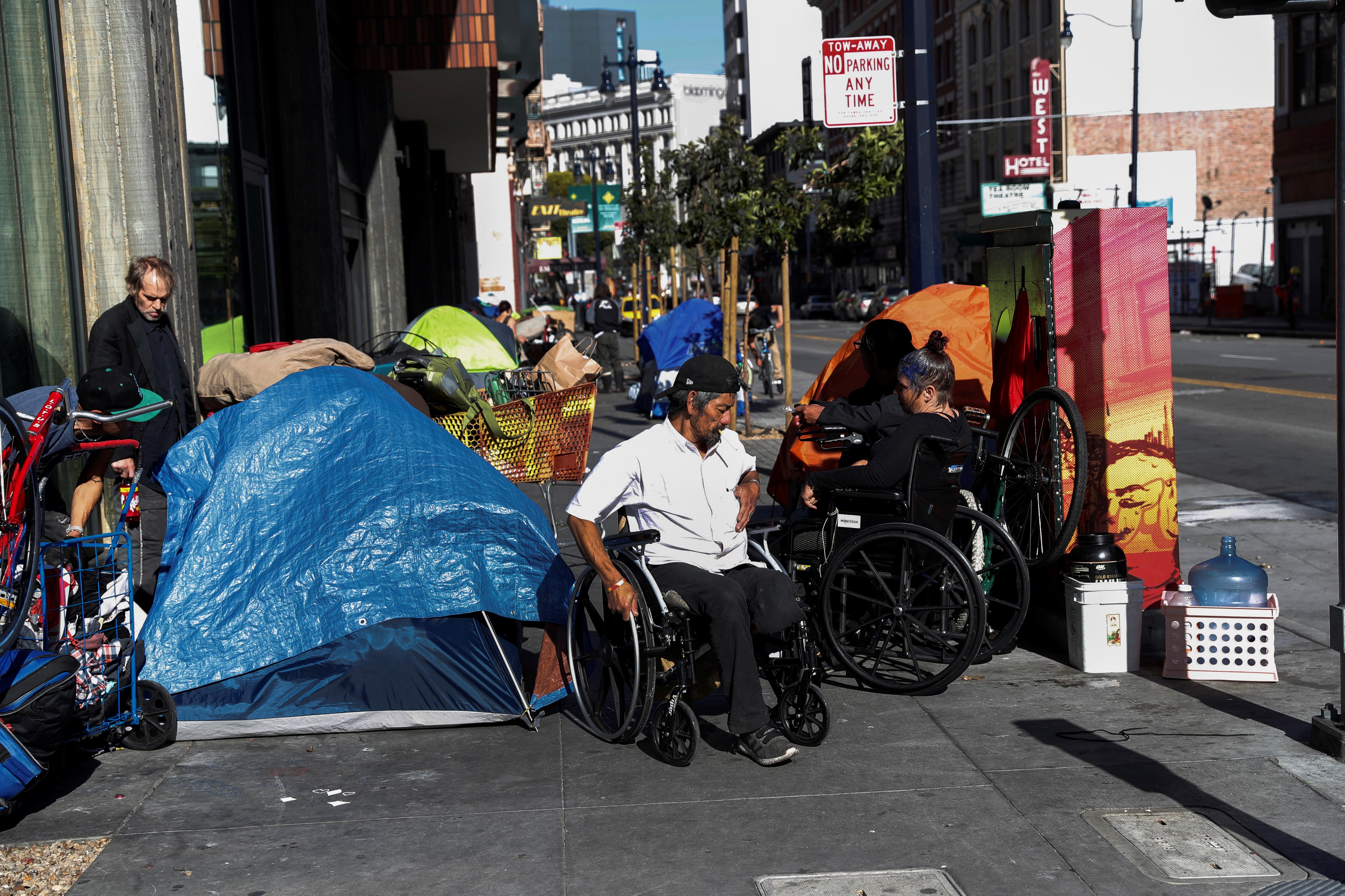 People including a man using a wheelchair near a makeshift tent