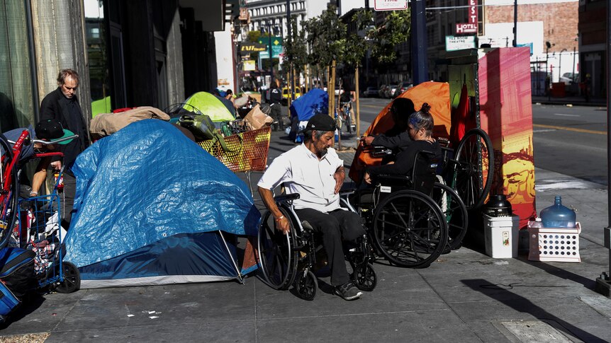 People including a man using a wheelchair near a makeshift tent