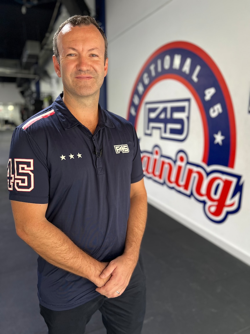Luke Armstrong stands in front of an F45 sign, wearing a blue branded polo shirt.