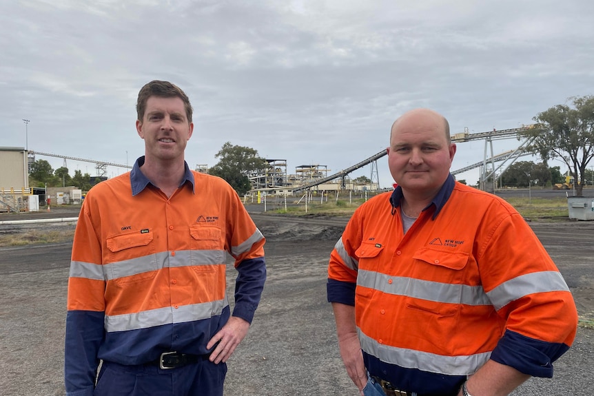 Two men in high visibility stand in front of coal mine 