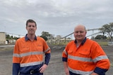 Two men in high visibility stand in front of coal mine 