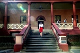 A woman with a red skirt walks up the front steps of NSW Parliament