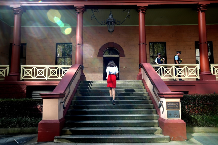 A woman with a red skirt walks up the front steps of NSW Parliament