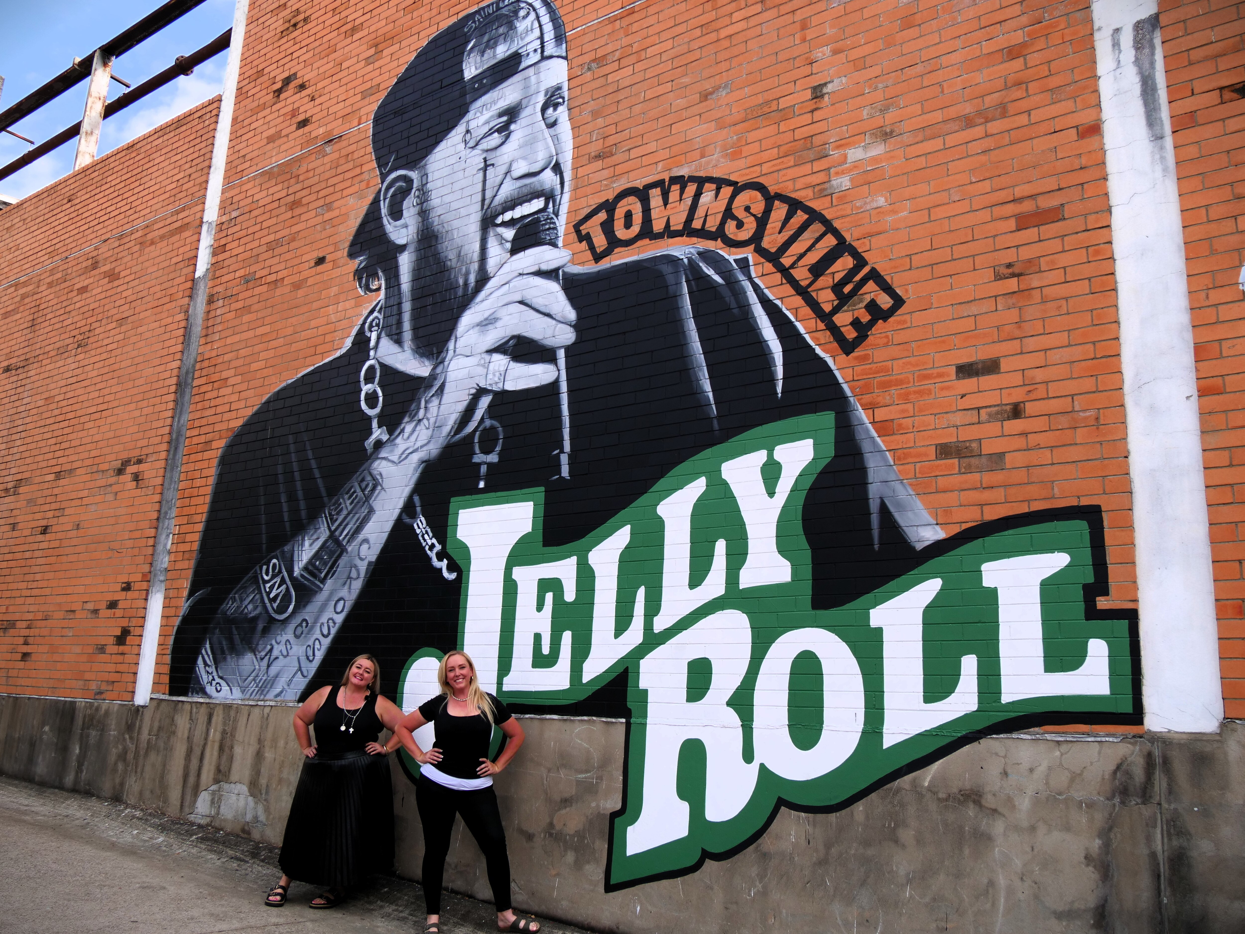 A large black and white painting of a male American singer holding a microphone with green font which says Jelly Roll.