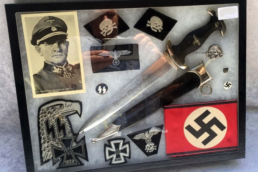 A framed collection of Nazi artefacts, including dagger, spear blade, badges, cloth patches and print of Third Reich Officer.