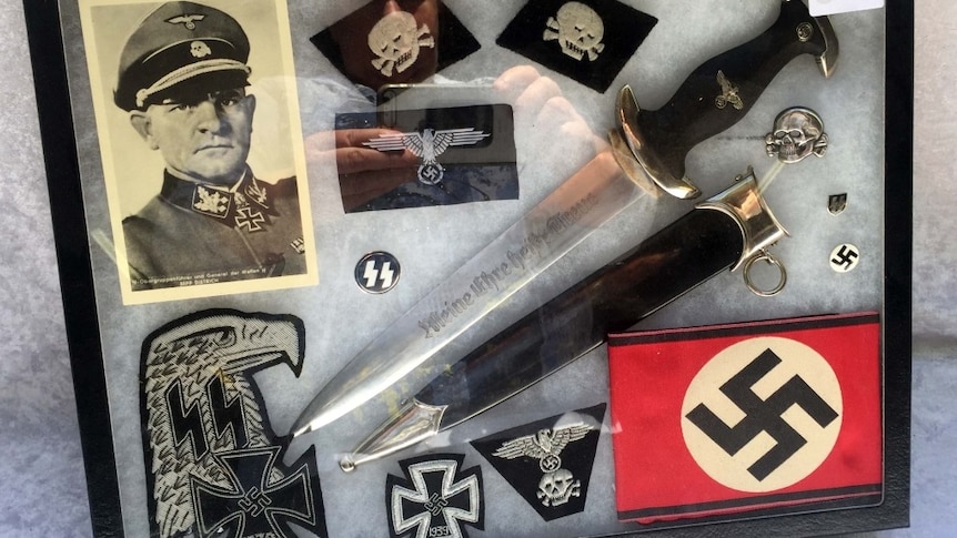 A framed collection of Nazi artefacts, including a dagger, spear blade, badges, cloth patches and print of Third Reich Officer.