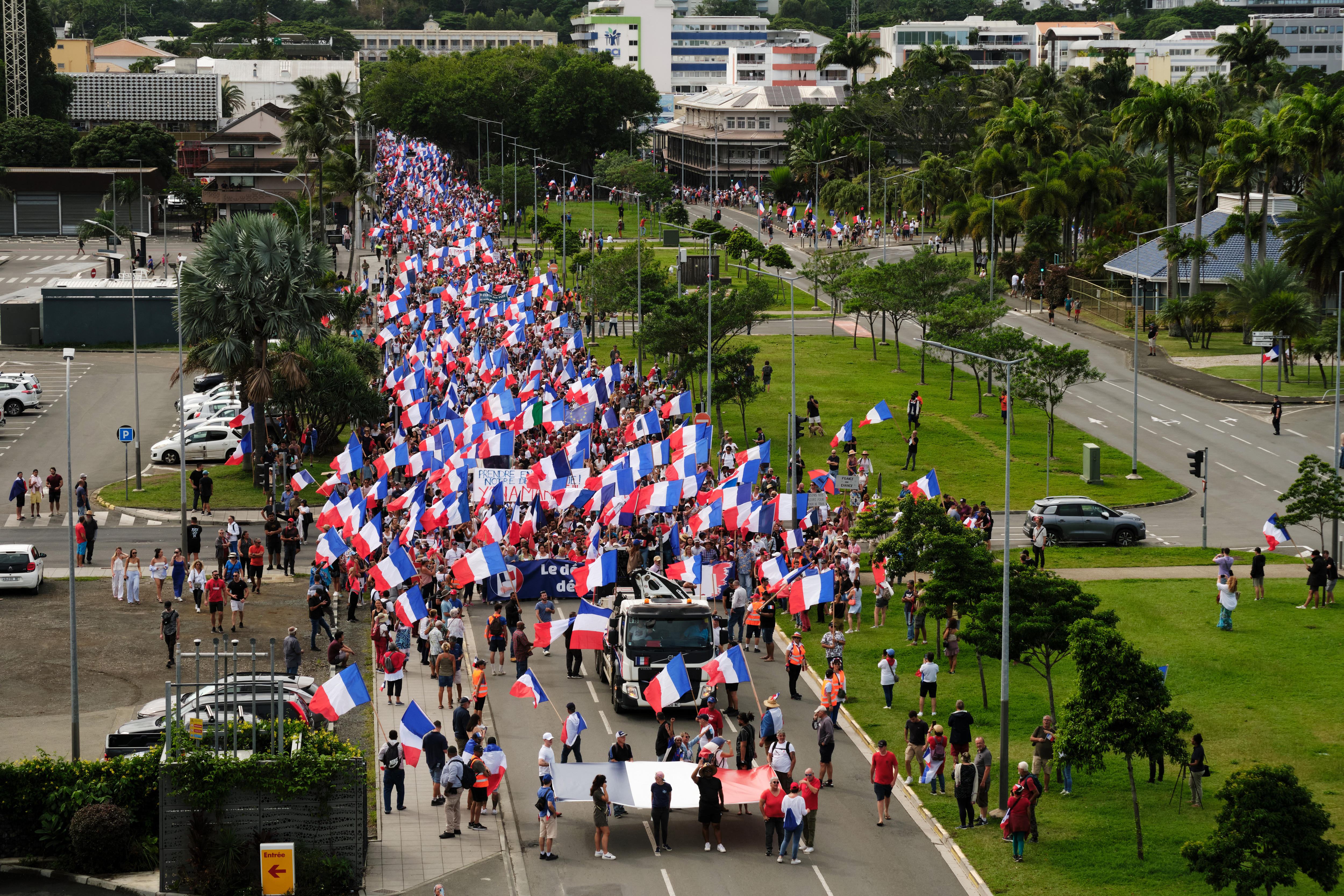 A large group of demonstrators parade waving French tricolour flags.