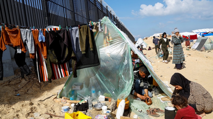 A man in seen inside a makeshift tent constructed from think plastic against the Rafah-Egypt border wall. 