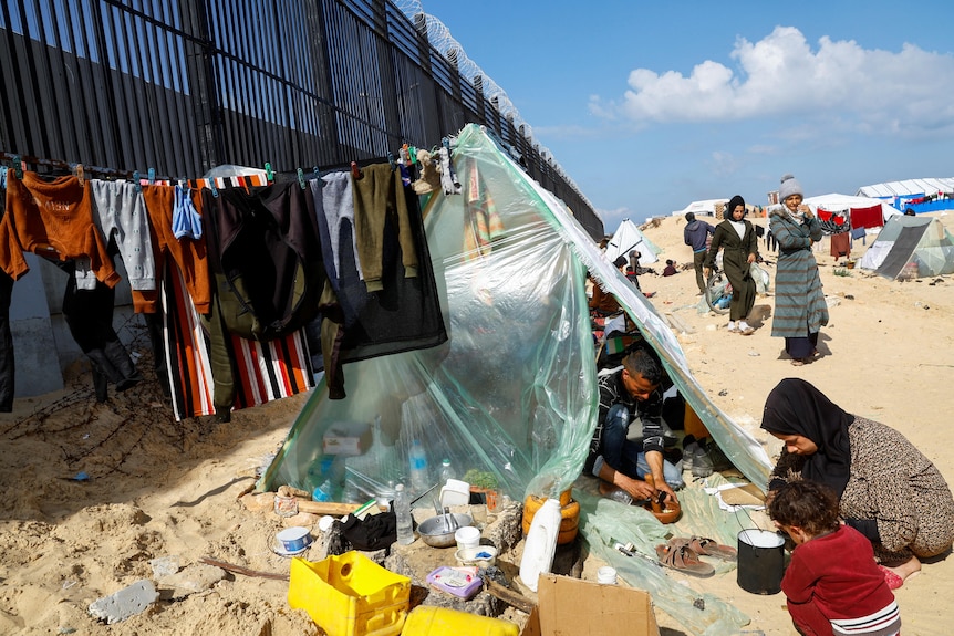 A man in seen inside a makeshift tent constructed from think plastic against the Rafah-Egypt border wall. 