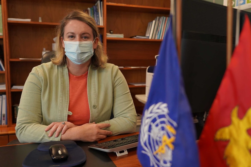 A woman in a face mask with blonde hair sits on