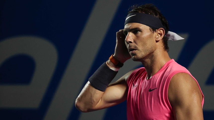 A serious-looking tennis player stands on court, staring into the distance.