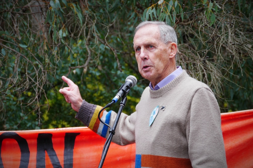 A man wearing a beige sweater stands behind a large red sign