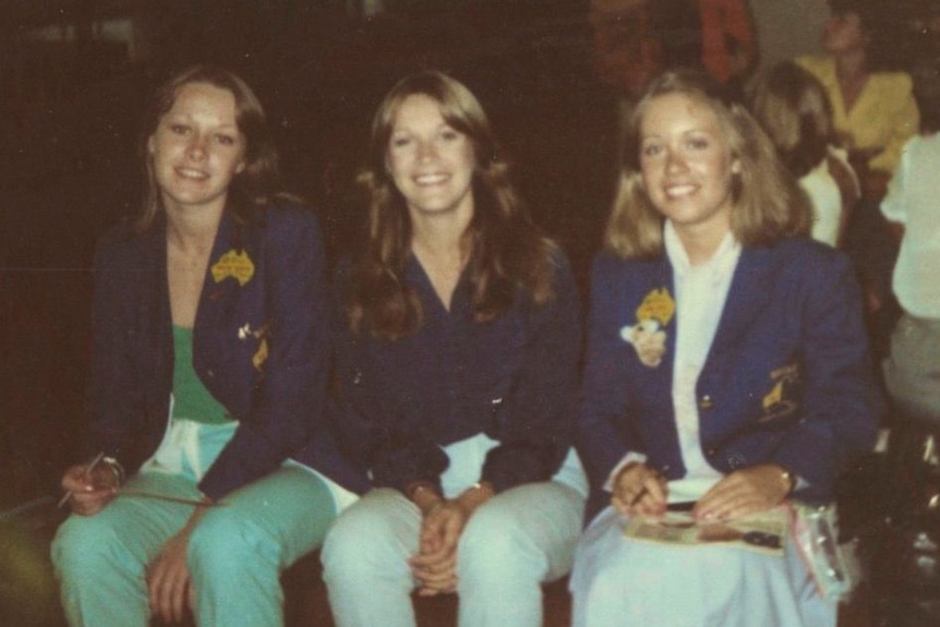 Three school girls sitting in uniforms.