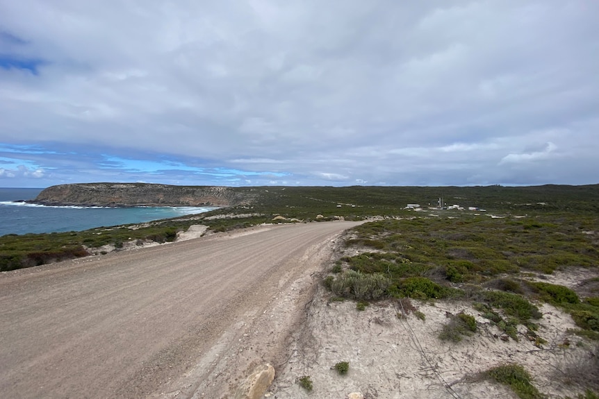 Coastal scene of ocean on left, road in the middle and rocket site in the distance on the right.