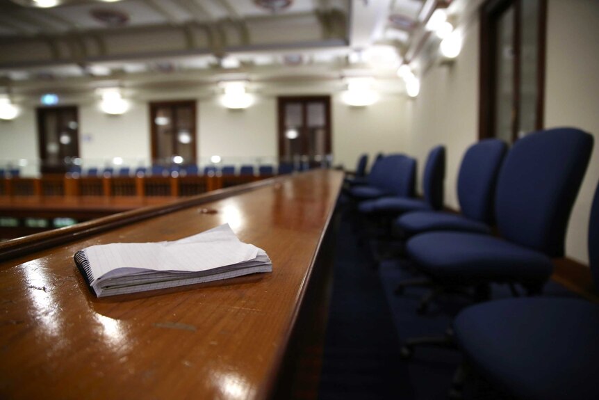 A notepad lies on the press gallery bench in the Lower House of the WA Parliament with blue chairs on the right.