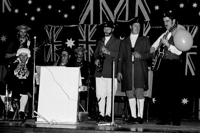 A band in sailor costumes play in front of Australian flags and Union Jacks