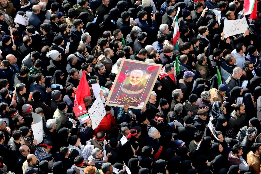 A large crowd gathered in a public square holding pictures of major general Soleimani