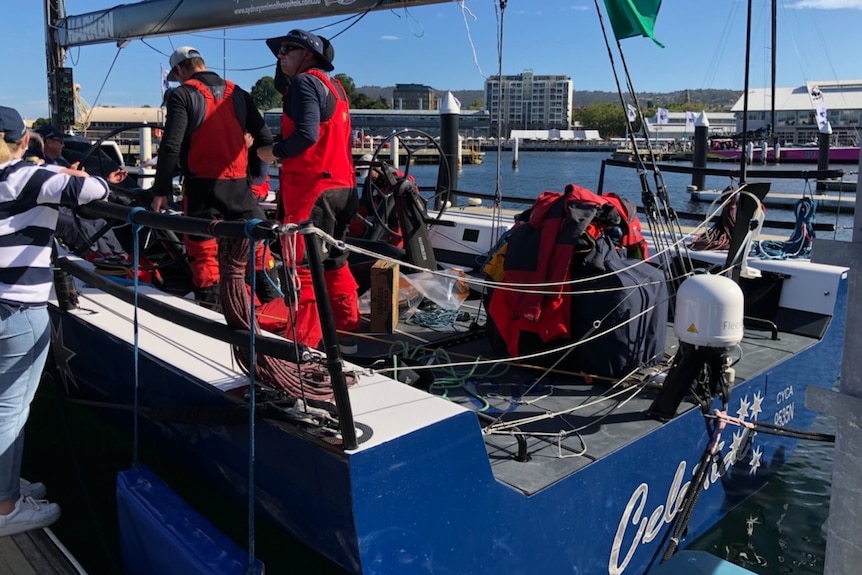 Crew members stand on a blue yacht at a dock