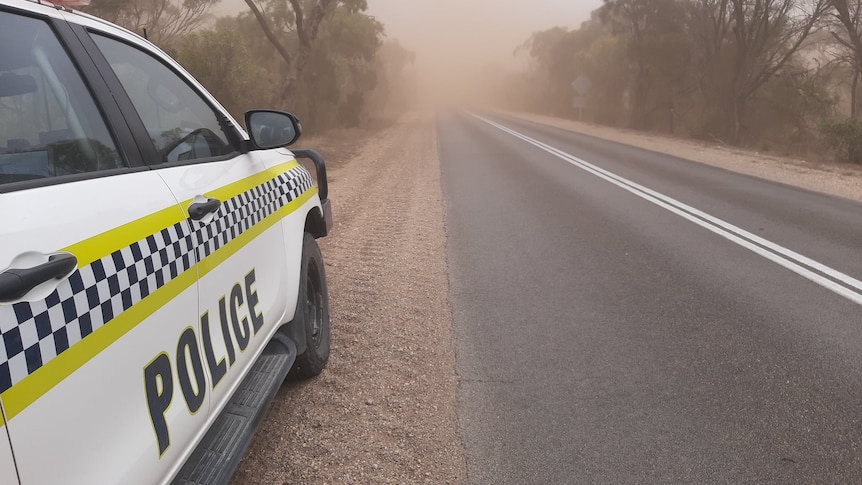 A police car parked on the side of a road as dust kicks up all around it