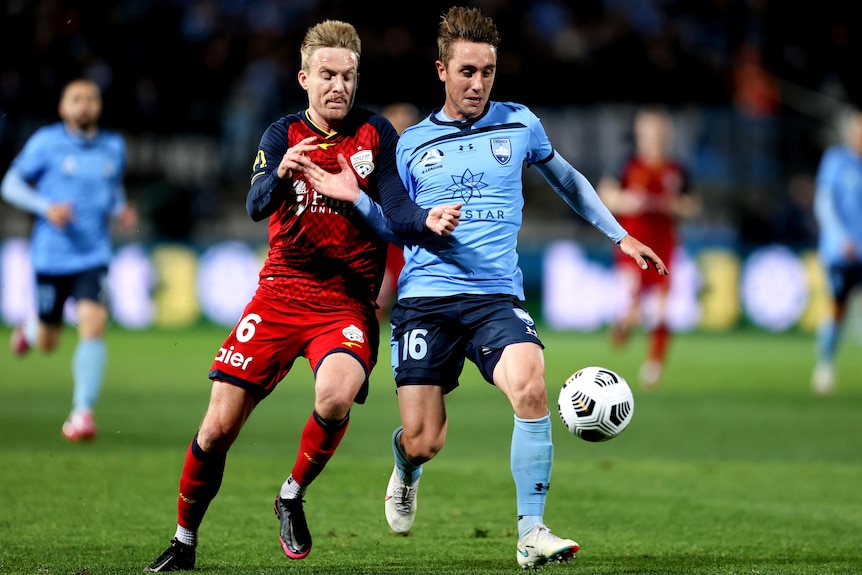 An Adelaide United A-League player and and a Sydney FC opponent contest for the ball. 