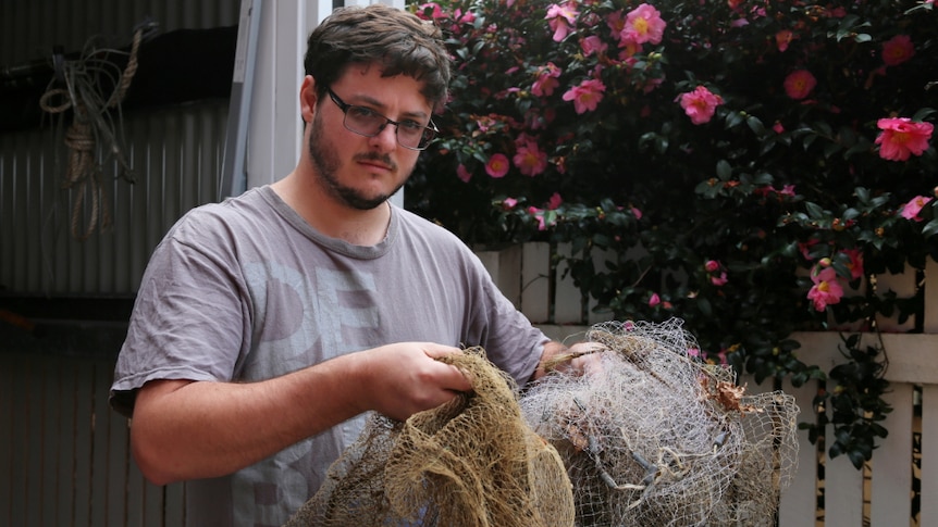 A man holds old casting nets in front of a shed.