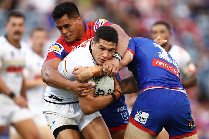 Penrith Panthers' Dallin Watene-Zelezniak looks to squirm out of a wrap tackle from two Newcastle Knights players