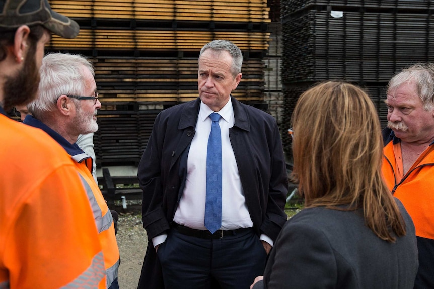 Bill Shorten, with his hands in his pockets, listens to men in high-vis jumpers. Justine Keay has her back to the camera