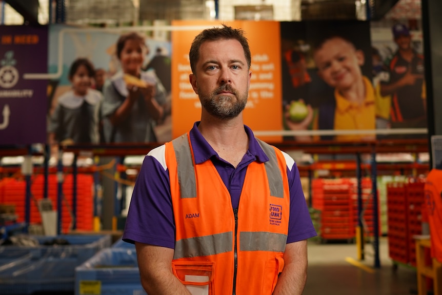 Man wearing a purple shirt and hi-vis orange vest standing in a warehouse.