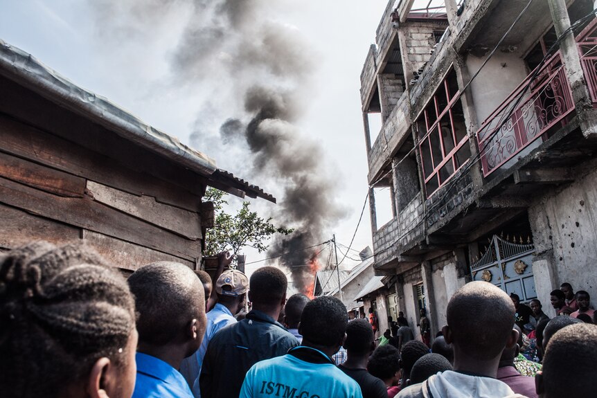 From within a crowd of Goma residents, you look up at a smoke plume billowing down a densely populated street.