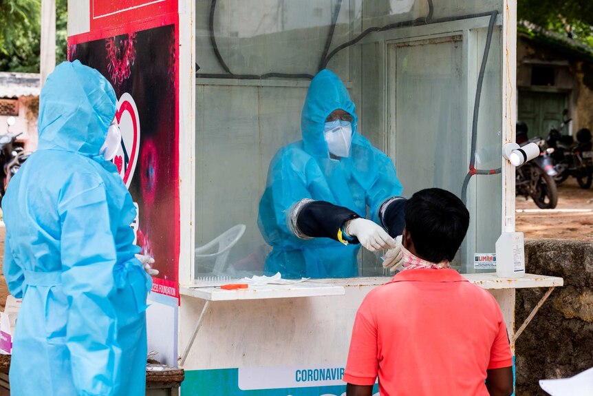 A health worker in full PPE testing someone for COVID-19 in a glass booth