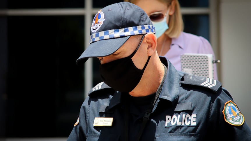 A man in a police uniform, cap and mask walks. 