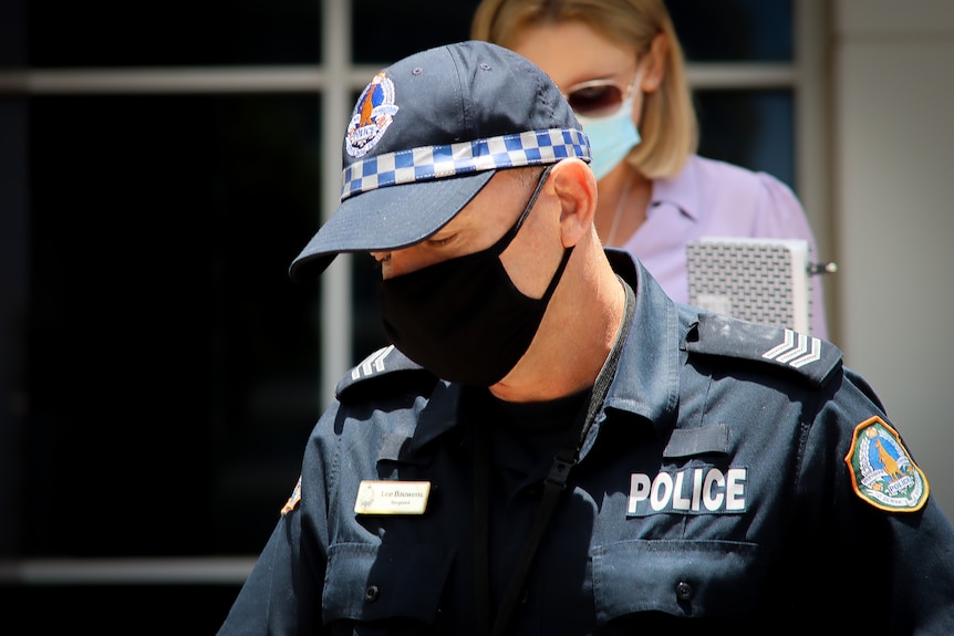 A man in a police uniform, cap and mask walks. 