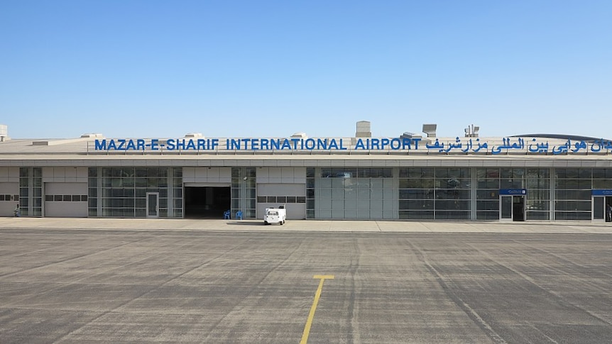A sign saying Mazar-e-Sharif International airport is displayed on top of a airport terminal.